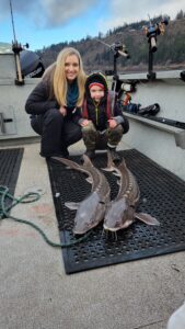 Two people showing off their caught sturgeon, which are lying on the dock.