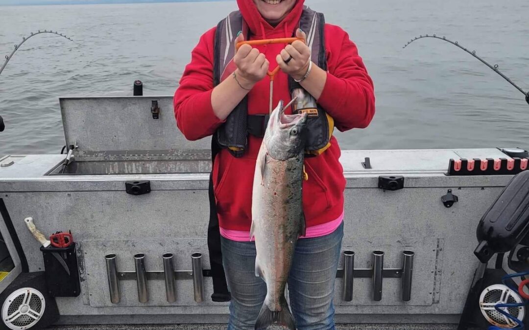 A girl on a boat holds a coho salmon she caught fishing in the Pacific Ocean off Astoria with Marvin's Guide Service.