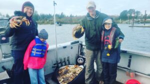 Two fathers hold Dungeness crabs while two children stand with them on the Marvin's Guide Service boat in the lower Columbia River. A large bag of crabs is on the boat deck.